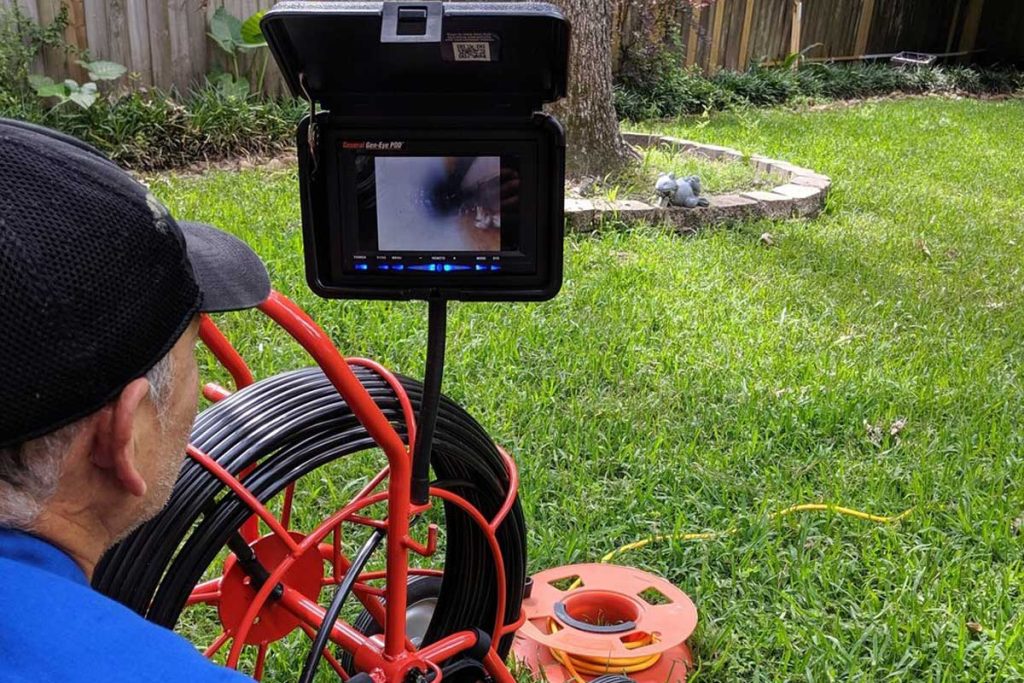 A plumber watching a sewer camera monitor while inspecting a yard line access point