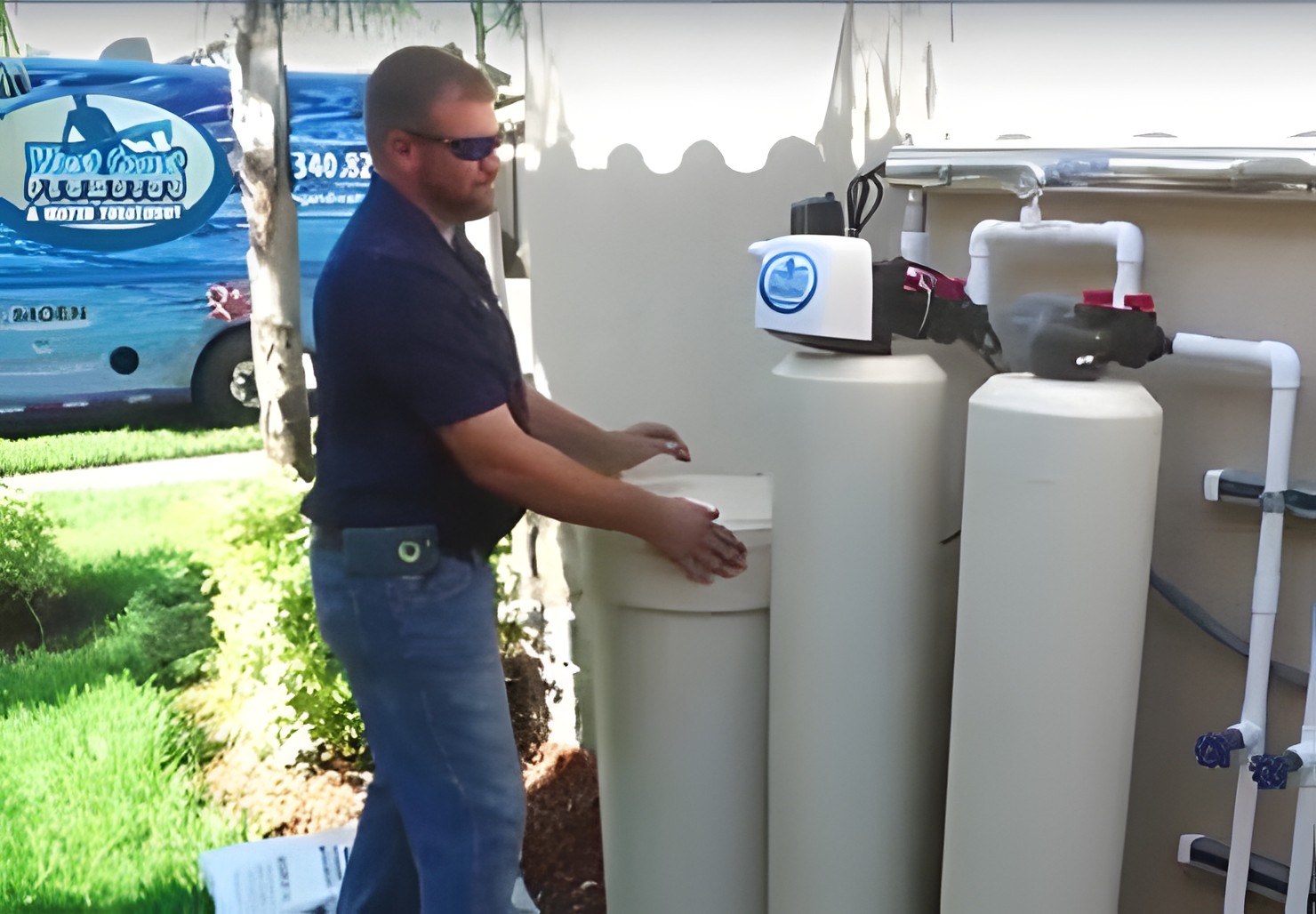A West Coast Plumbing technician servicing a whole-house water treatment system beside a customer's home